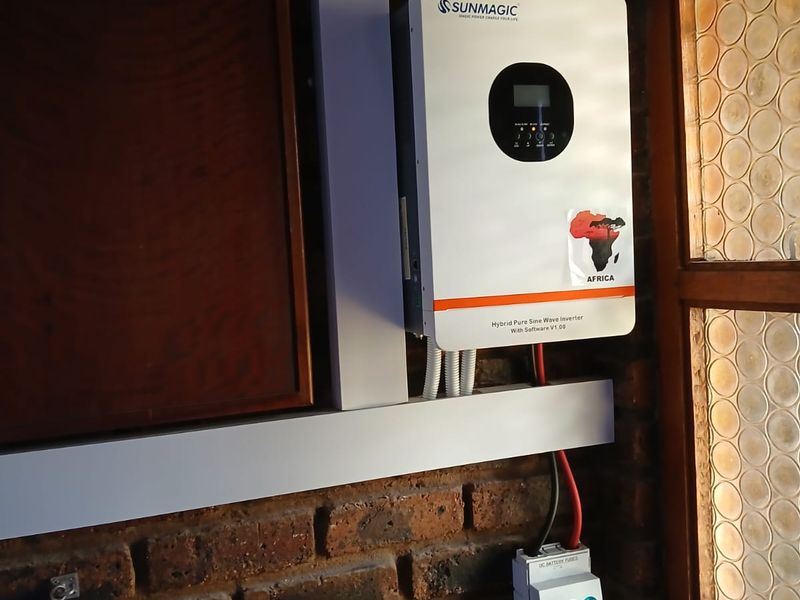 A wall-mounted Sunmagic hybrid inverter and DC battery fuse unit installed on an exposed brick wall.