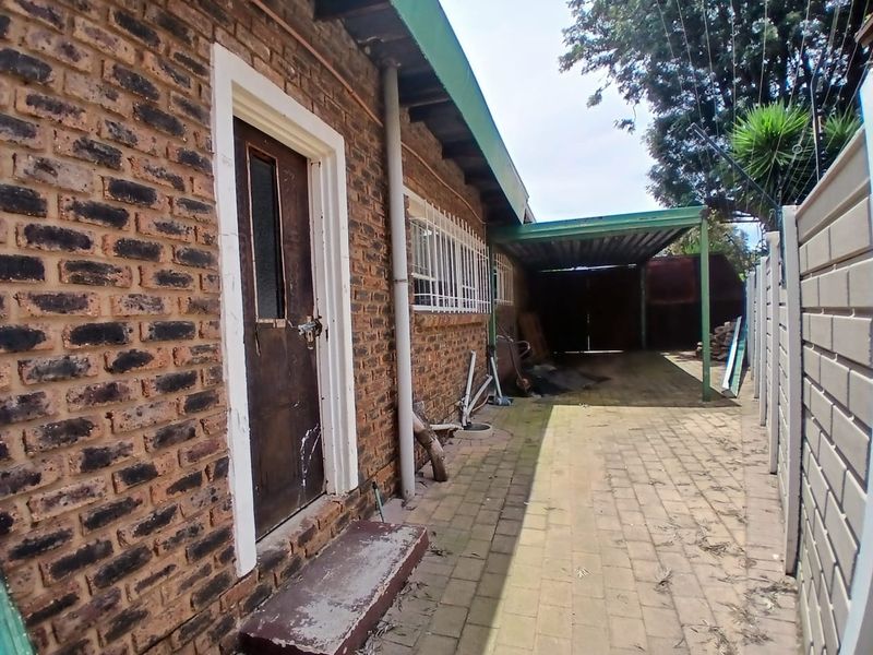 Rear exterior view of the property featuring a face brick facade, paved driveway, and a covered carport area.