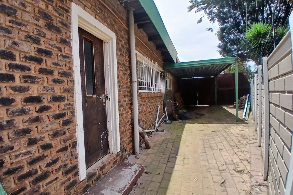 Rear exterior view of the property featuring a face brick facade, paved driveway, and a covered carport area.