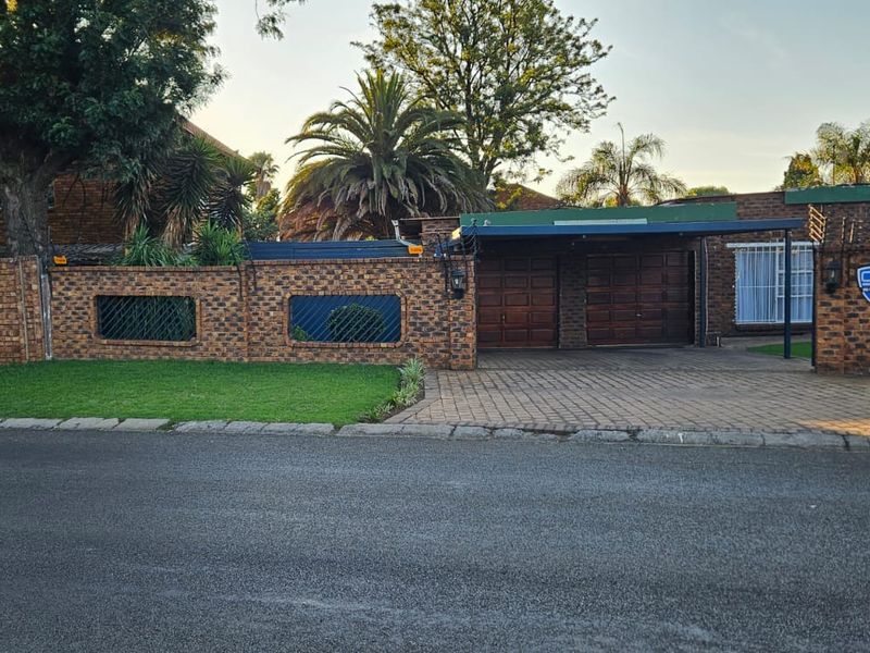 Front view of a brick-faced residential property featuring a double garage, paved driveway, carport, and secure boundary wall with electric fencing.