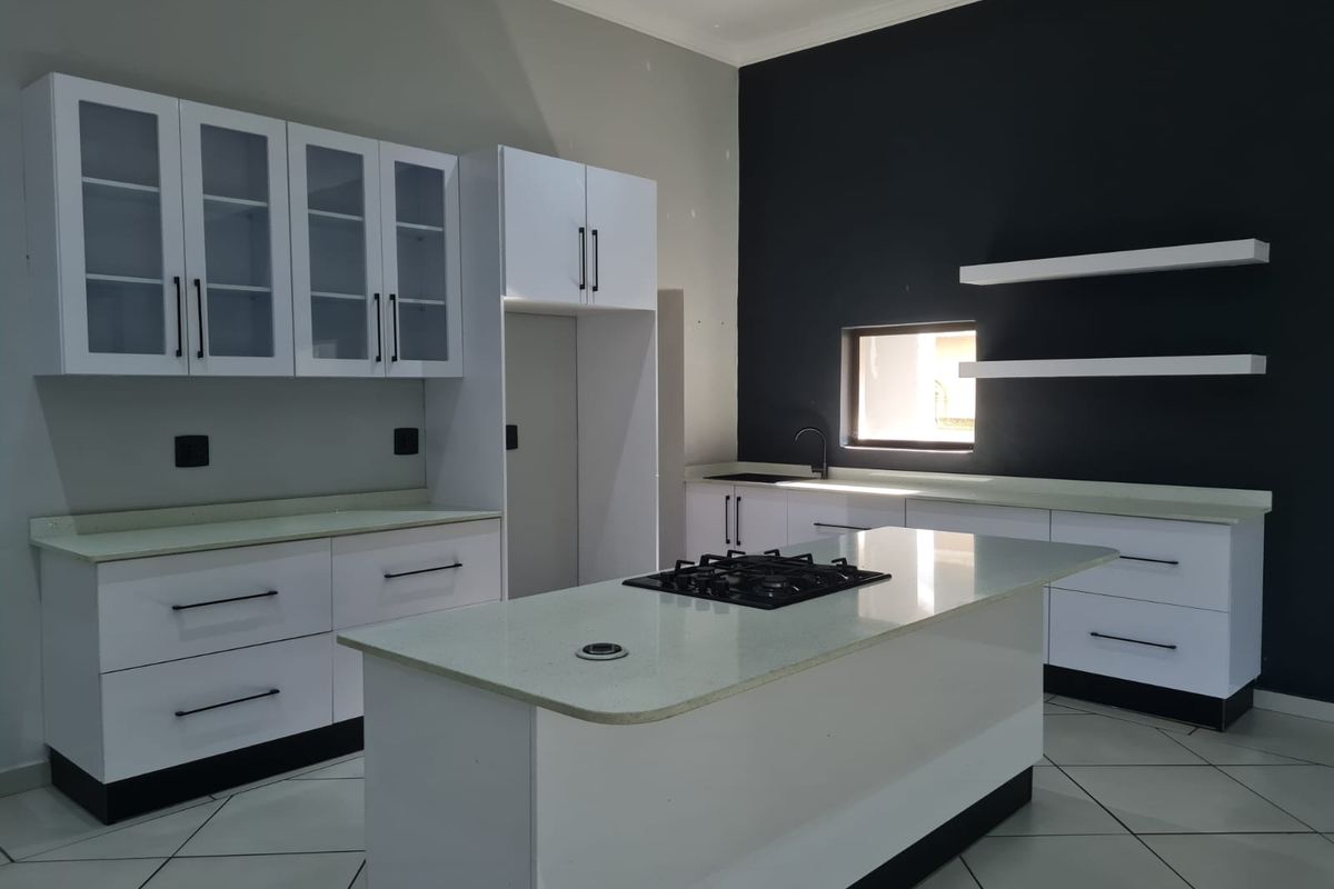 Modern kitchen featuring white cabinetry, a central island with a built-in gas hob, stone countertops, and contrasting dark feature wall.
