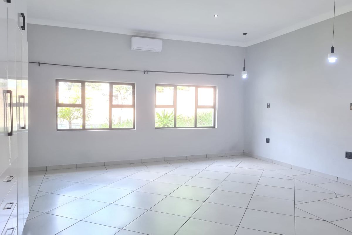 A bright, spacious, and empty living area featuring tiled flooring, recessed lighting, pendant lights, and a wall-mounted air conditioning unit.