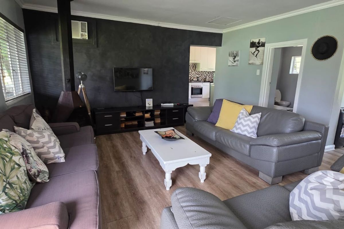 A comfortable living room featuring wood-look flooring, a central fireplace, and an open-plan layout leading to the kitchen and bathroom areas.
