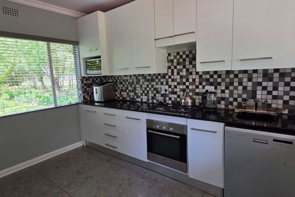 Modern kitchen featuring white cabinetry, black granite countertops, a gas hob, built-in oven, and a striking black and white mosaic tiled backsplash.