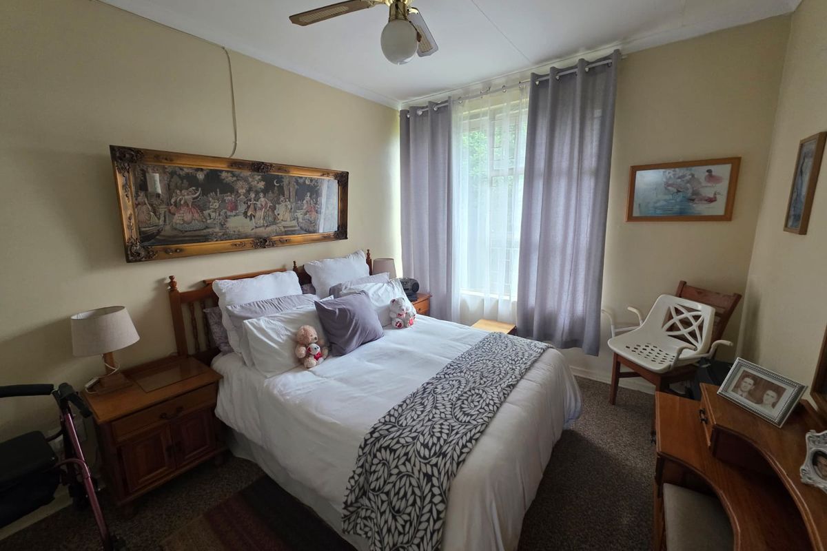 A standard bedroom featuring a ceiling fan, carpeted flooring, and a window with curtain tracks.