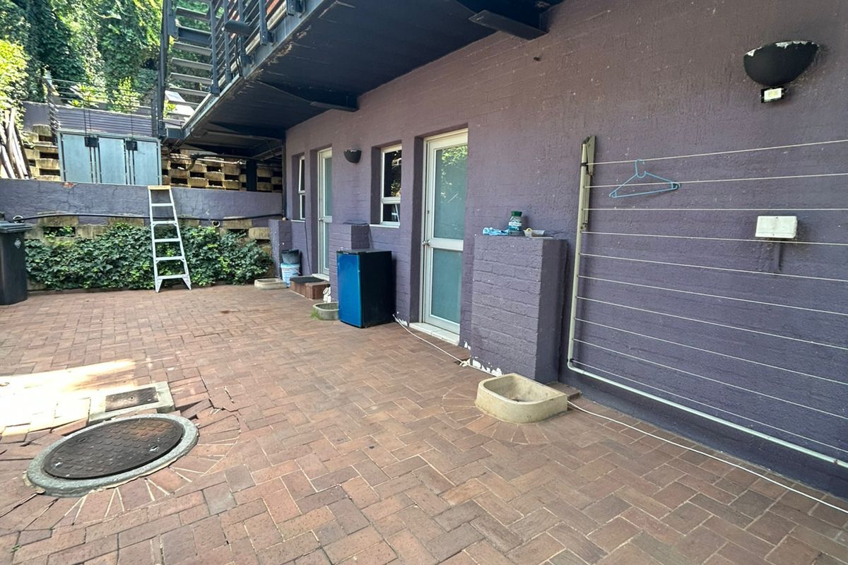 Rear exterior area featuring brick paving, a metal staircase, and wall-mounted utility fixtures, showing signs of wear and maintenance requirements.