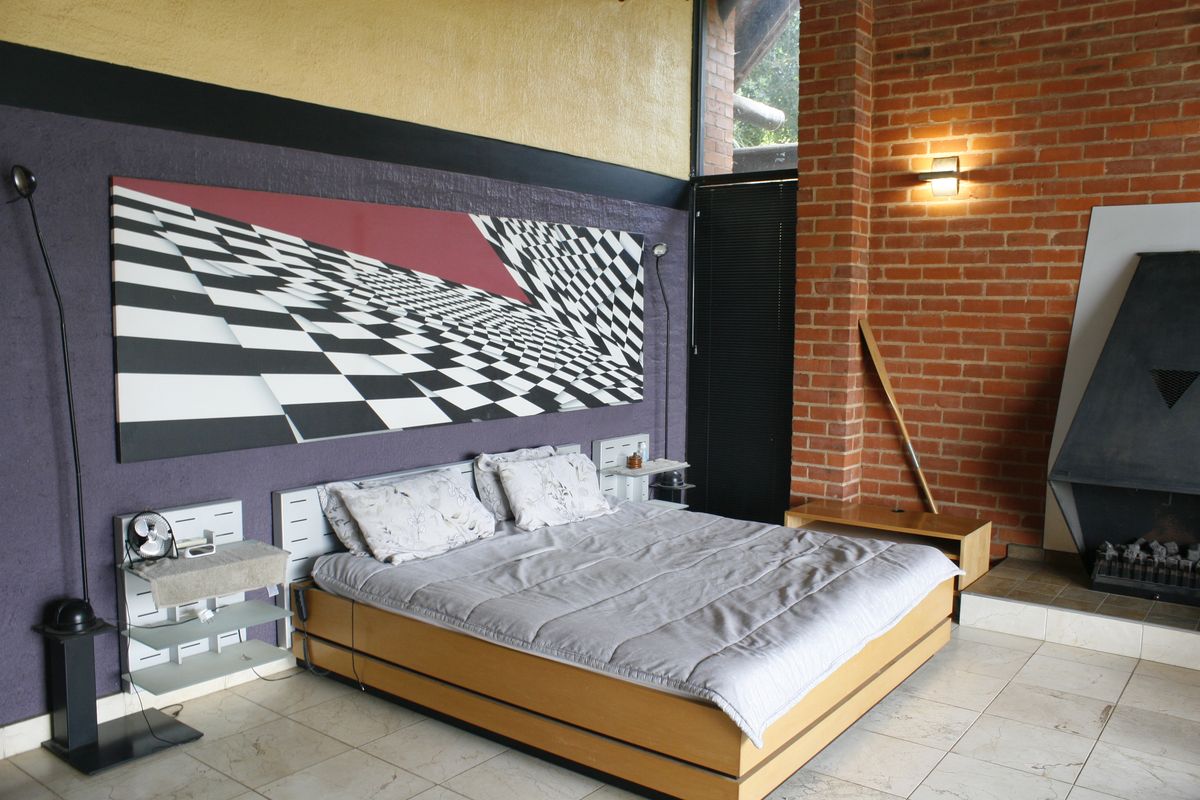 Spacious bedroom featuring exposed brick walls, tiled flooring, and a built-in fireplace, offering a unique architectural aesthetic with high-level windows.