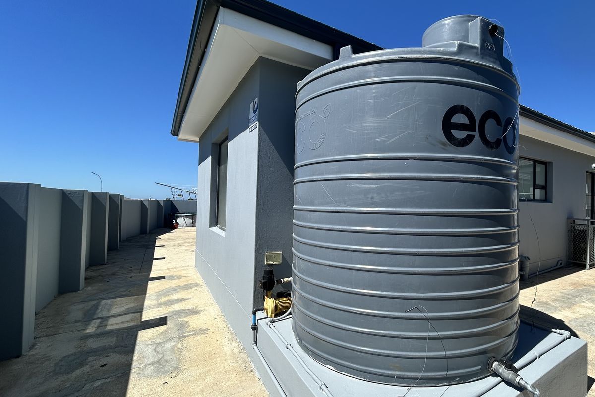 Exterior view of the property side featuring a large grey water storage tank with an integrated pump system on a concrete base.