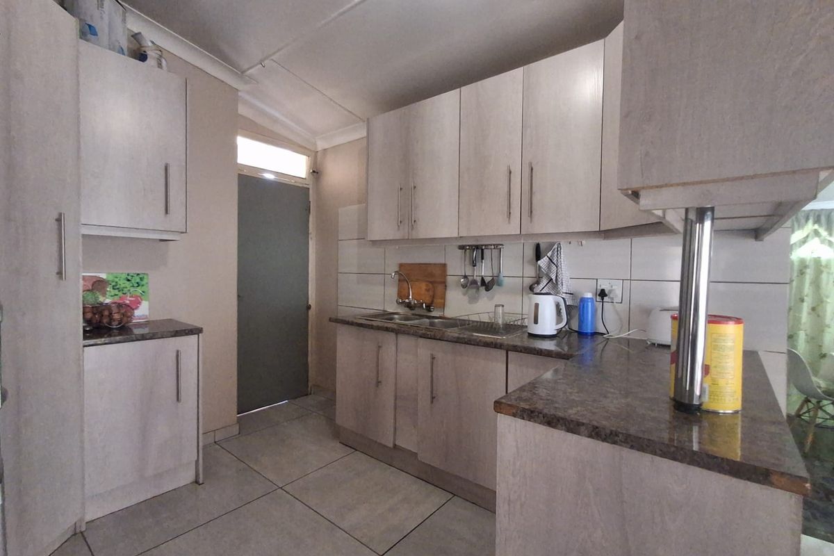 A functional kitchen featuring light-toned cabinetry, laminate countertops, tiled flooring, and a stainless steel sink, providing a practical workspace.