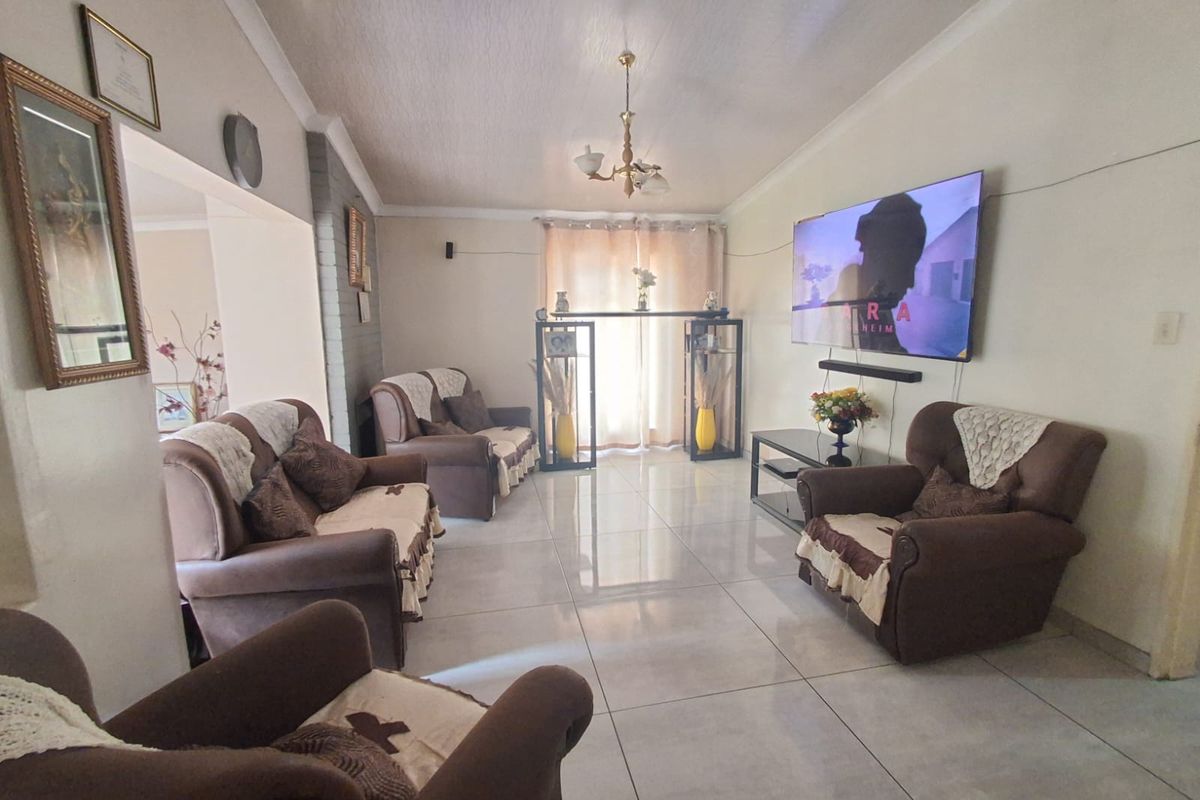 A spacious living room featuring large format floor tiles, a textured ceiling, and a central chandelier, providing a comfortable and functional family living space.