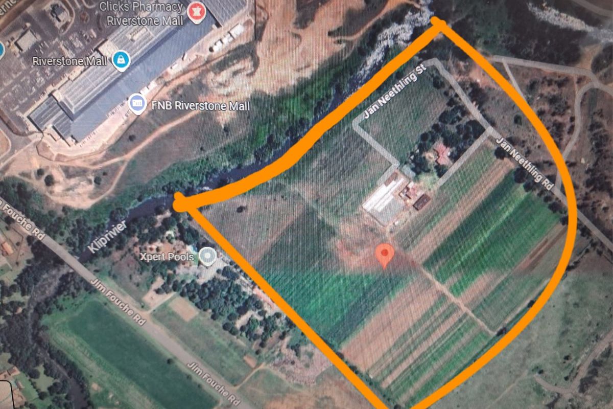 Aerial view of a large vacant residential plot featuring river frontage and proximity to local commercial amenities.