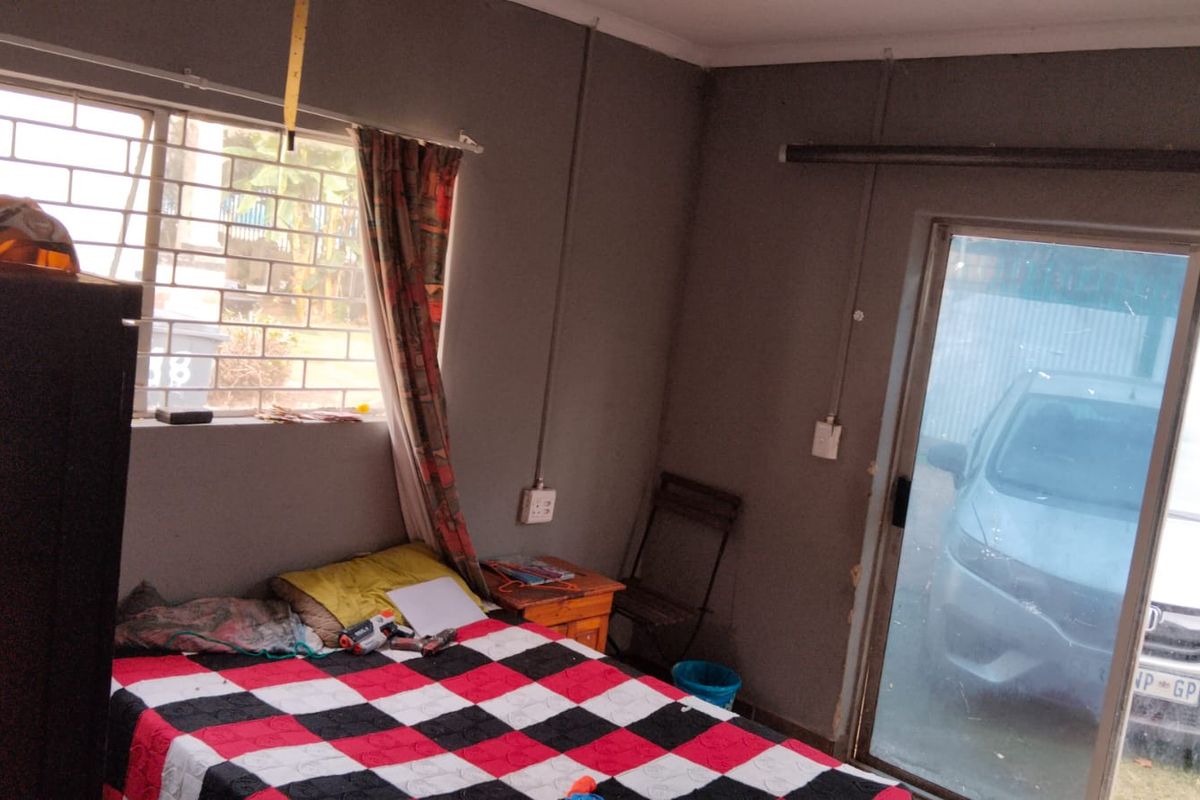 A bedroom featuring a sliding glass door, security bars on the window, and exposed electrical conduit along the walls.