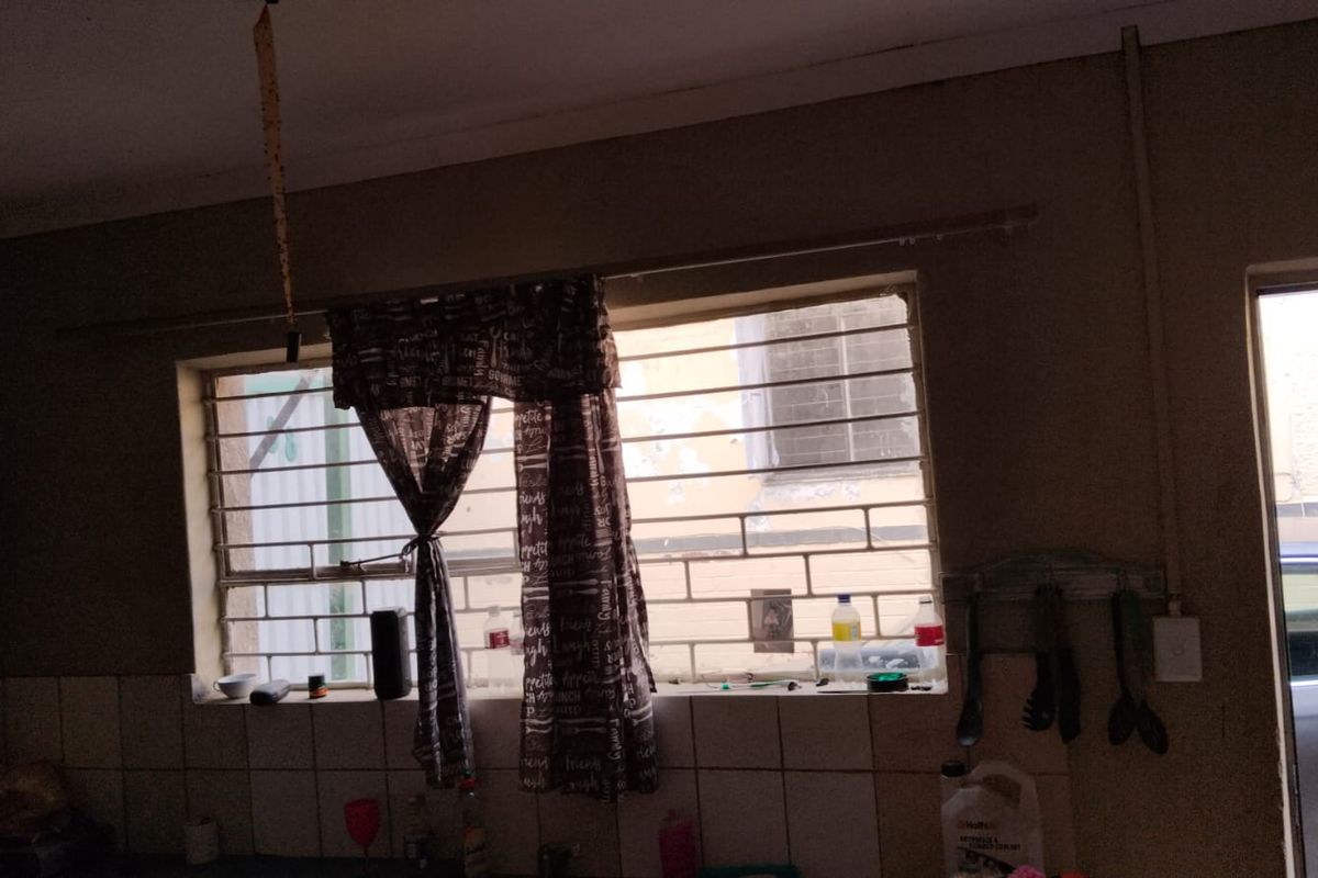 A kitchen area featuring a window with security bars and tiled splashback, showing signs of wear and dated finishes.