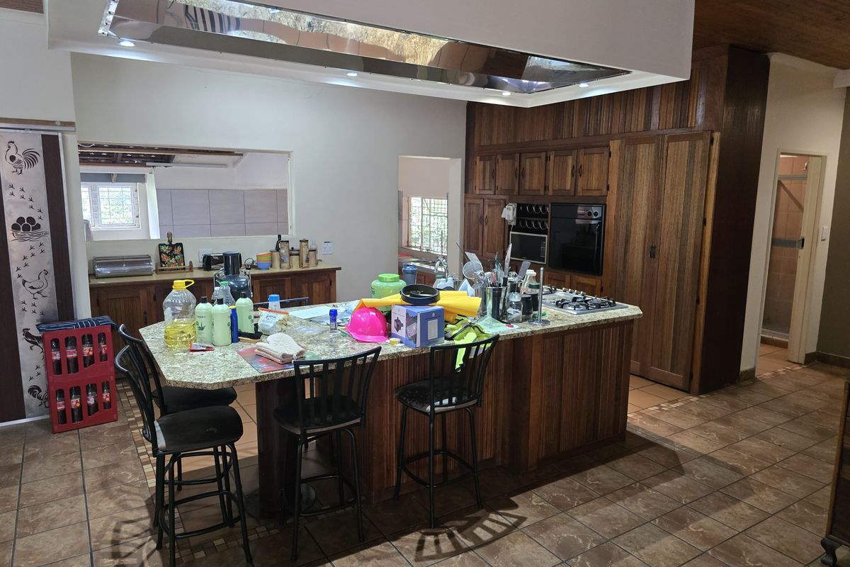 Spacious kitchen featuring a large central island with granite countertops, built-in oven, gas hob, and extensive wooden cabinetry.