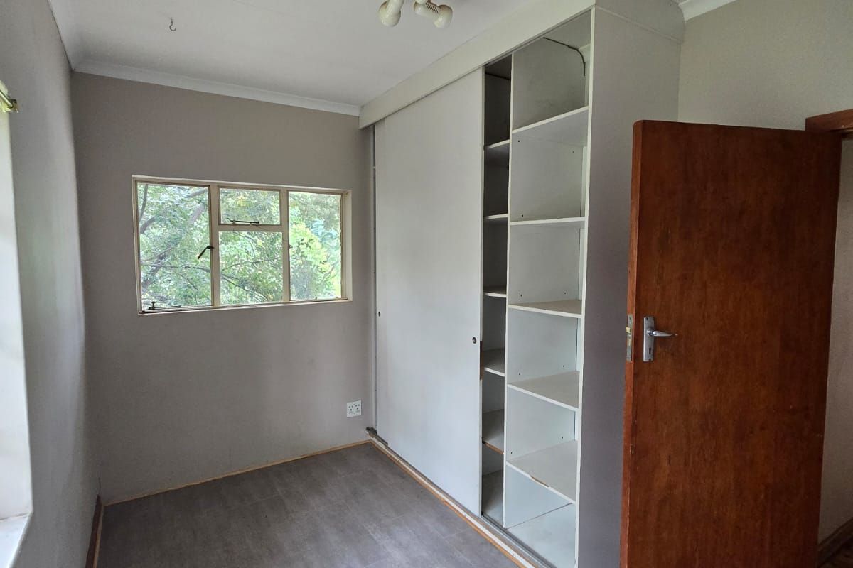A bedroom featuring built-in shelving and wardrobe storage, neutral wall finishes, and wood-look flooring.