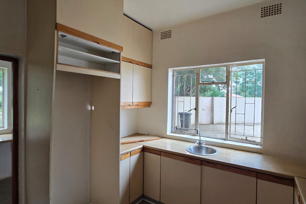 A dated kitchen featuring original cabinetry, a single basin sink, and a window overlooking the exterior. The space is ready for a modern renovation.