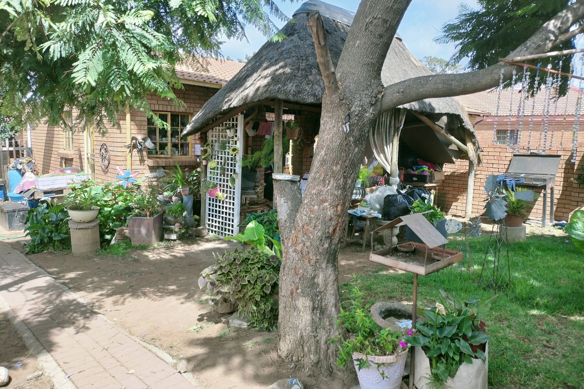A rear garden area featuring a thatched lapa structure, brick paving, and established trees, providing a rustic outdoor space.