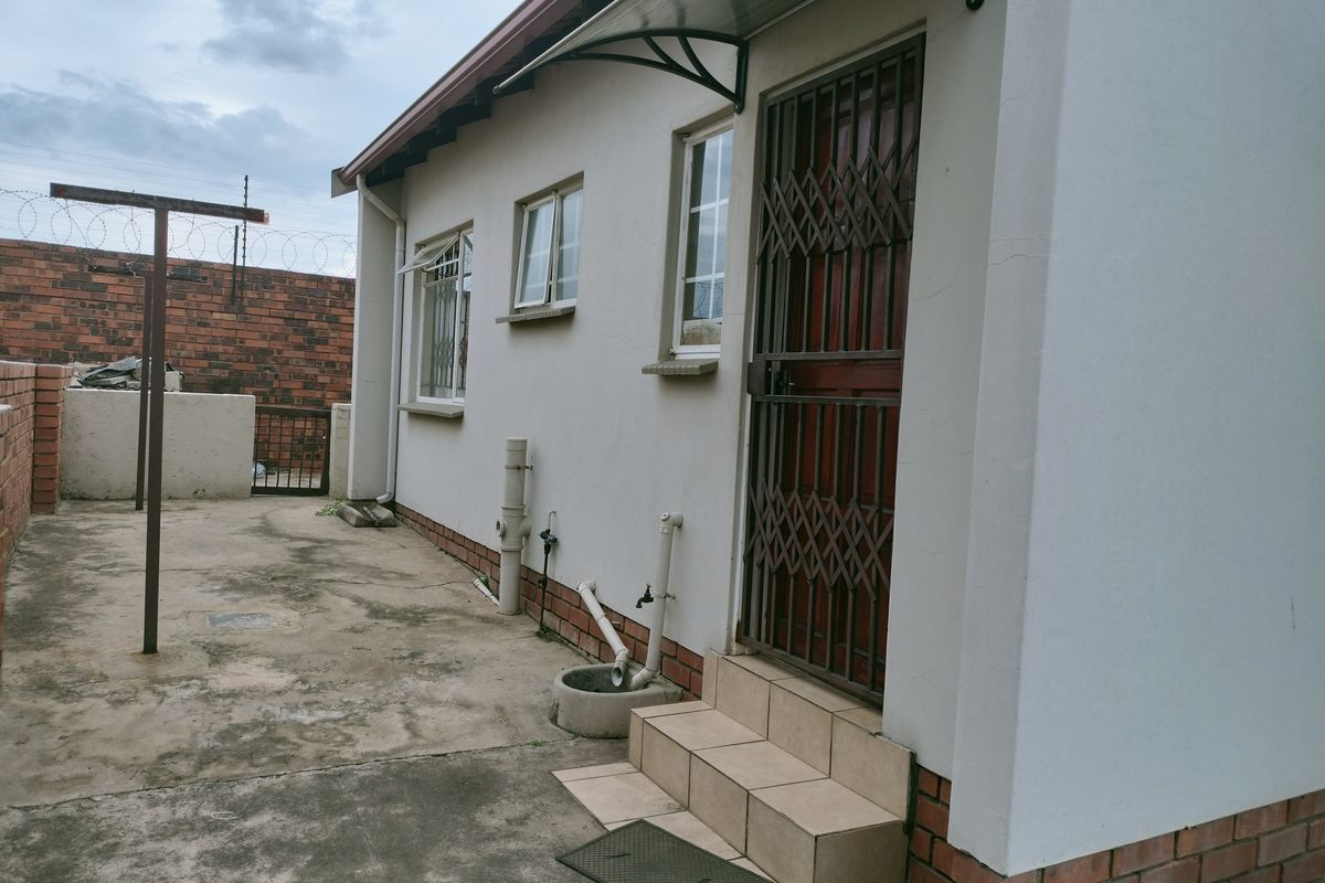 Rear exterior view of the property featuring a paved courtyard, security gate, and external plumbing fixtures.