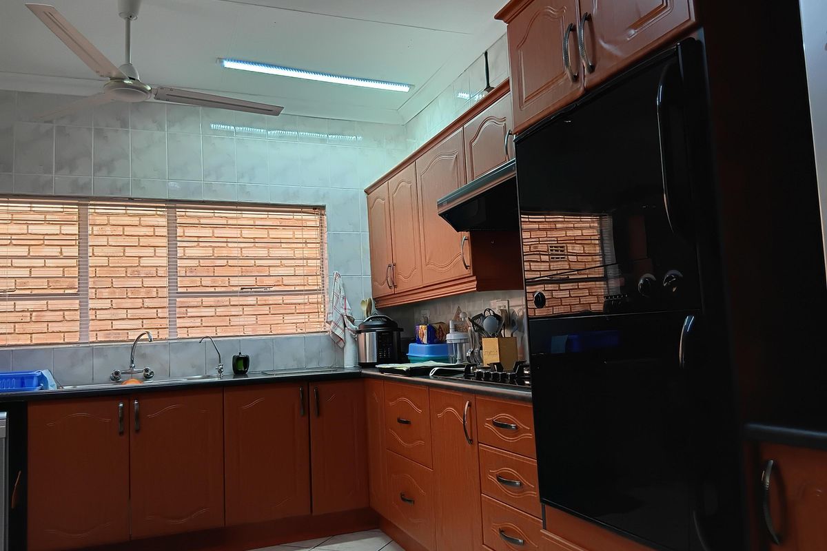 A functional kitchen featuring traditional wood-finish cabinetry, built-in oven, extractor fan, tiled backsplash, and a double sink with a window view.