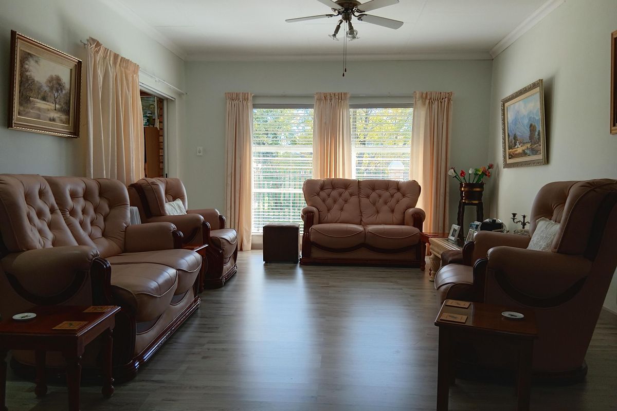 A well-maintained living room featuring modern laminate flooring, a central ceiling fan, and large windows that provide ample natural light.