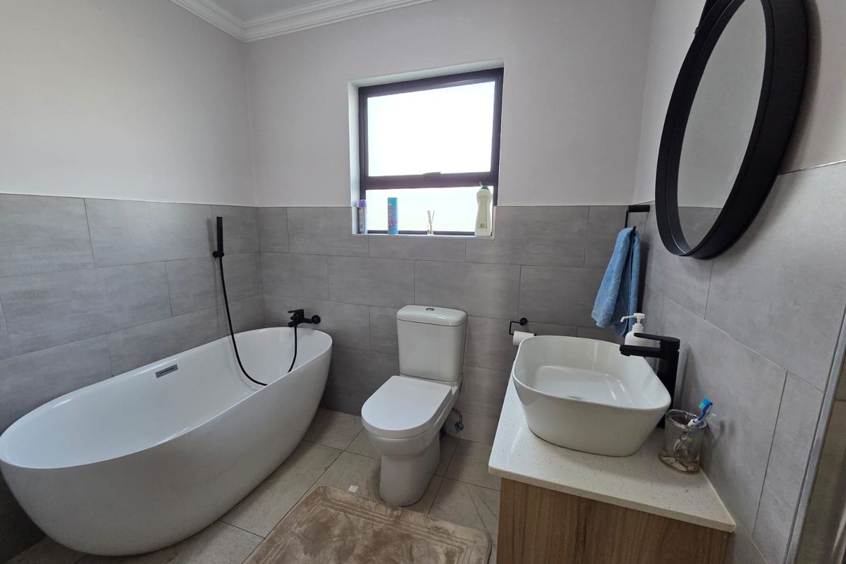 Modern bathroom featuring a freestanding bathtub, a contemporary vessel sink vanity, a toilet, and neutral grey wall tiling.