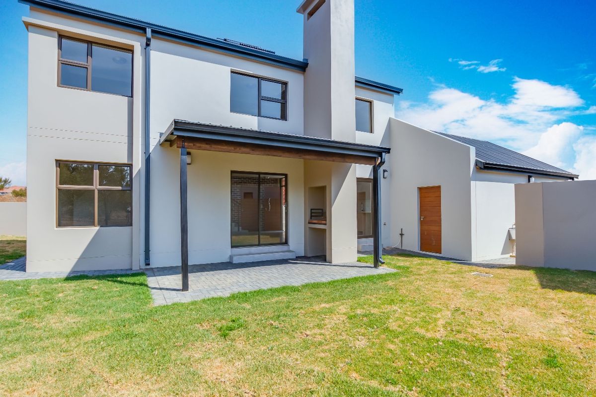Rear view of the modern two-story house featuring a covered patio with a built-in braai, paved area, and a private garden.