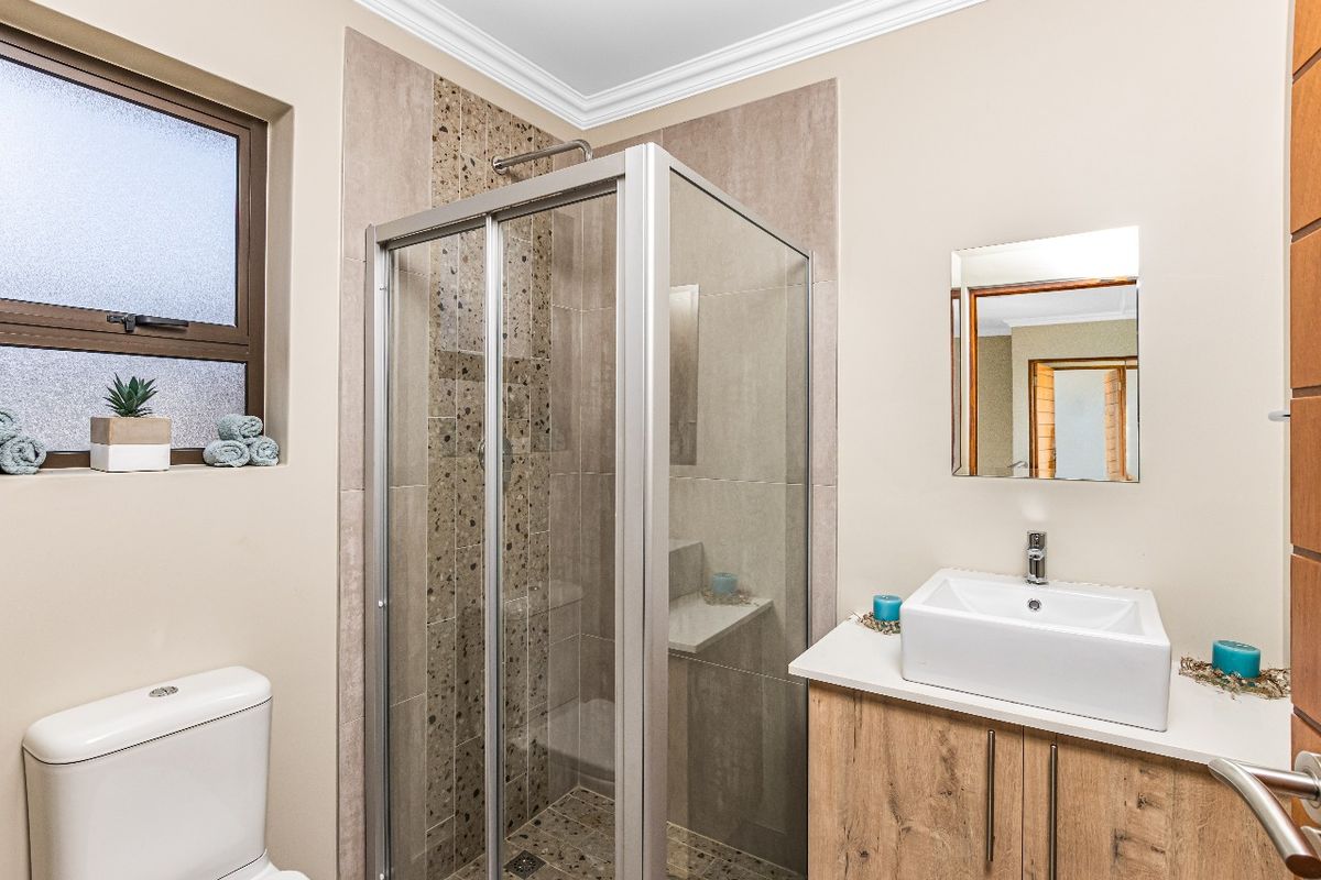 A modern bathroom featuring a glass-enclosed shower with mosaic tile accents, a vanity with a vessel sink, and a toilet.