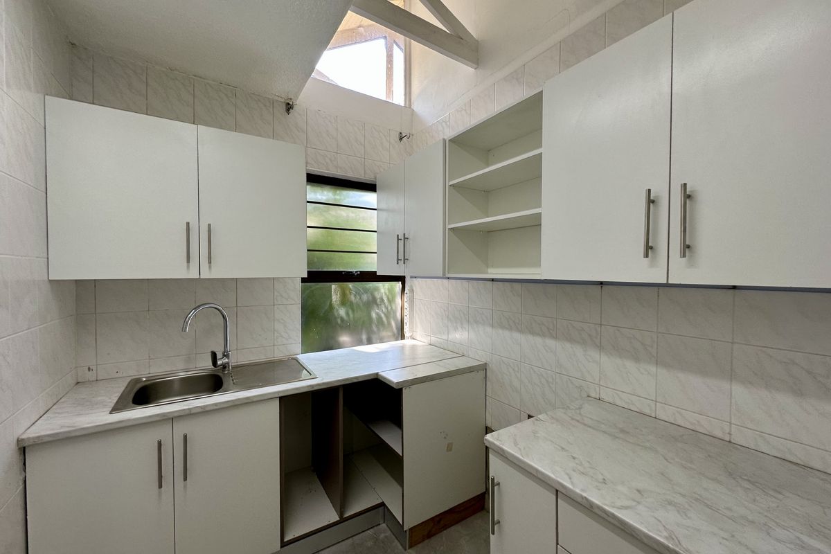 A functional kitchen featuring white cabinetry, marble-effect countertops, a stainless steel sink, and high vaulted ceilings with natural light.