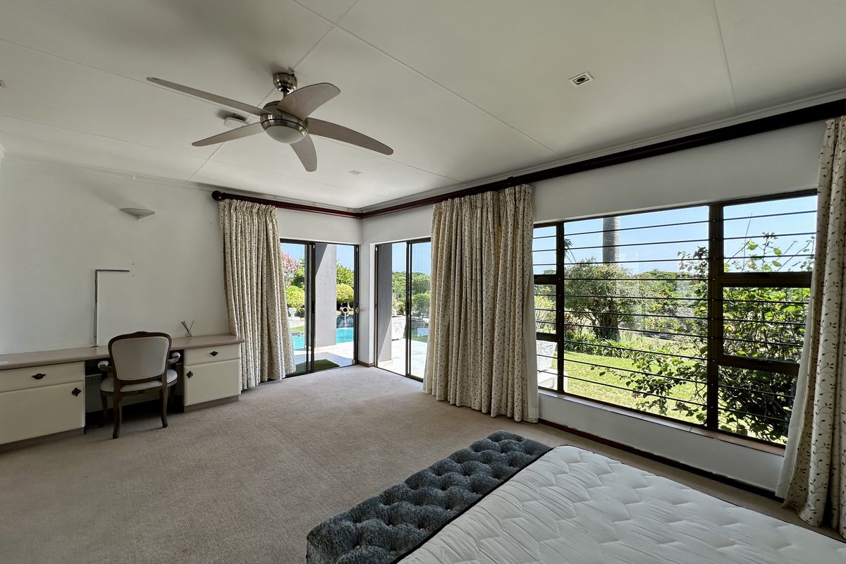 Spacious bedroom featuring a built-in desk, ceiling fan, and large windows with garden views and direct access to the outdoor pool area.