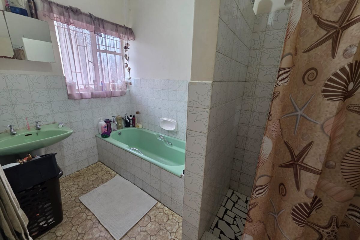 A dated bathroom featuring a green bathtub and matching basin, tiled walls, and a separate shower area with a privacy wall.