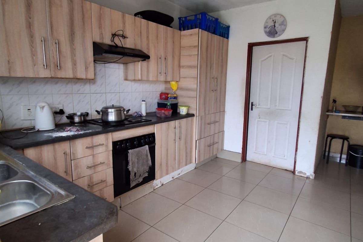 A functional kitchen featuring light wood-grain cabinetry, a built-in oven with extractor fan, and tiled flooring, requiring some cosmetic maintenance.