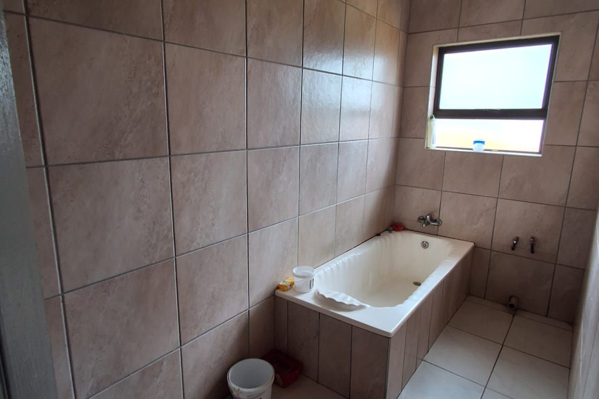 A bathroom featuring floor-to-ceiling tiled walls, a built-in bathtub, and tiled flooring, awaiting final fixture installation.
