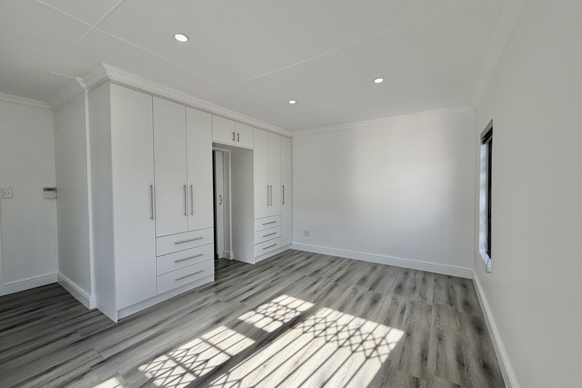 A bright, modern bedroom featuring neutral walls, high-quality laminate flooring, and extensive built-in cabinetry with integrated storage.