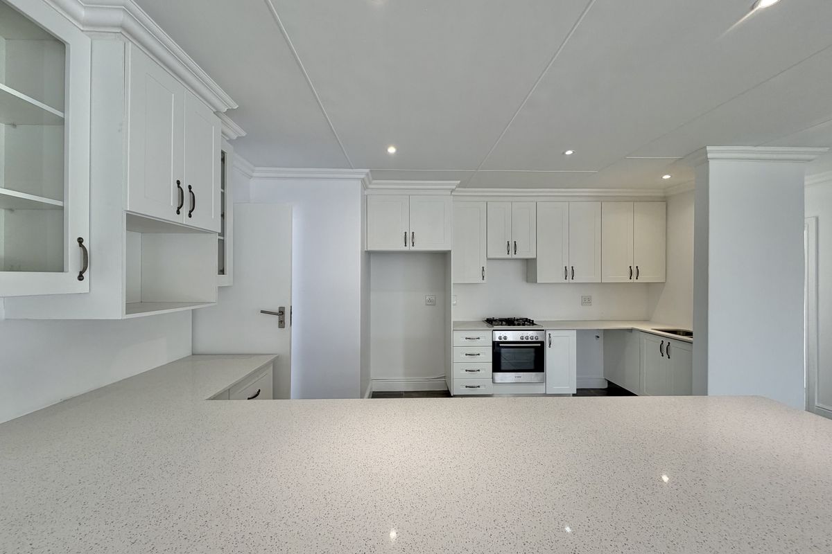 A clean, modern kitchen featuring white shaker-style cabinetry, quartz countertops, and a built-in oven with gas hob, presented in excellent condition.