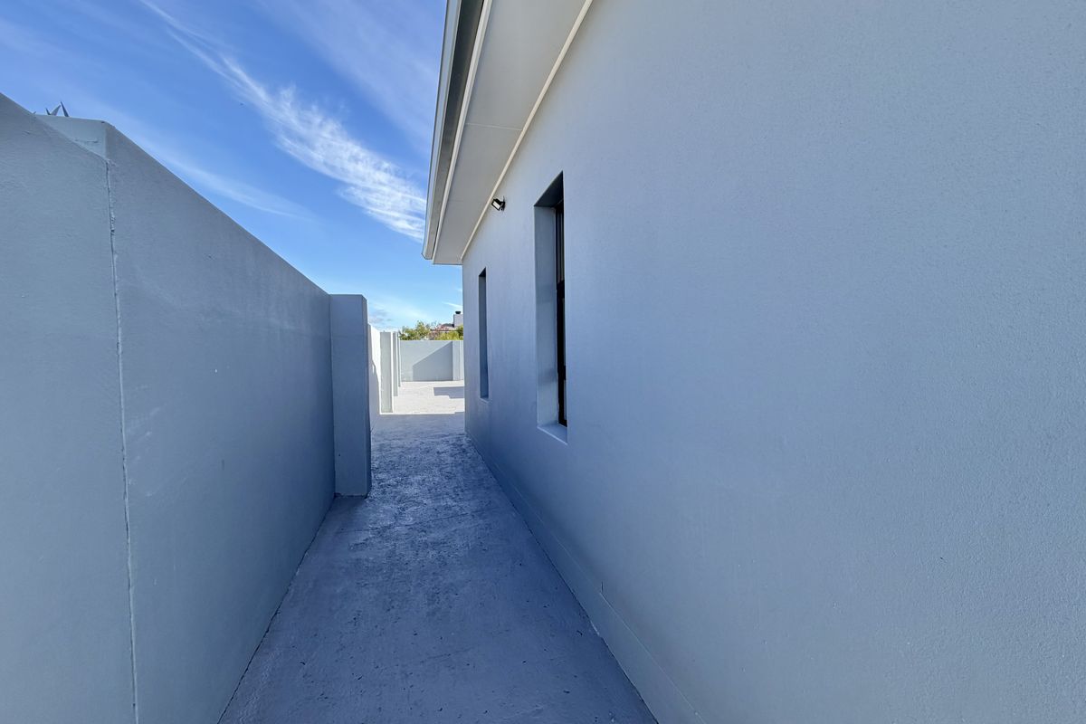 A clean, narrow side passage featuring smooth painted exterior walls, a concrete pathway, and modern external lighting.