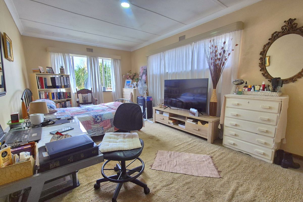 A spacious bedroom featuring carpeted flooring, large windows with curtains, and a functional layout suitable for a sleeping and study area.