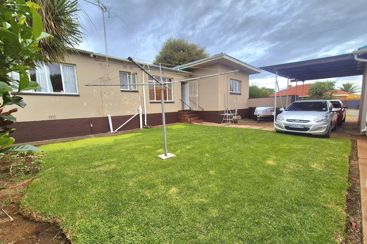 Rear view of the property featuring a lawn, a covered carport area, and exterior wall access with visible signs of wear.