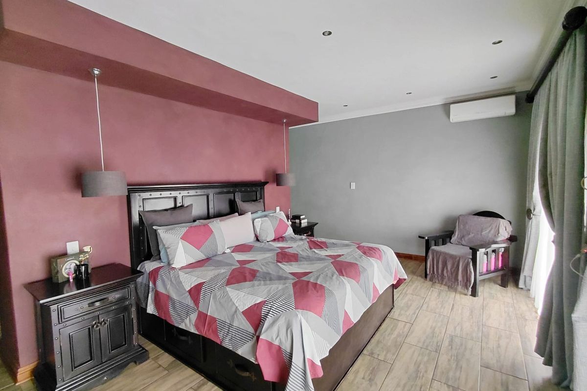 Spacious bedroom featuring wood-look tiled flooring, a feature wall with integrated bulkhead lighting, and a wall-mounted air conditioning unit.
