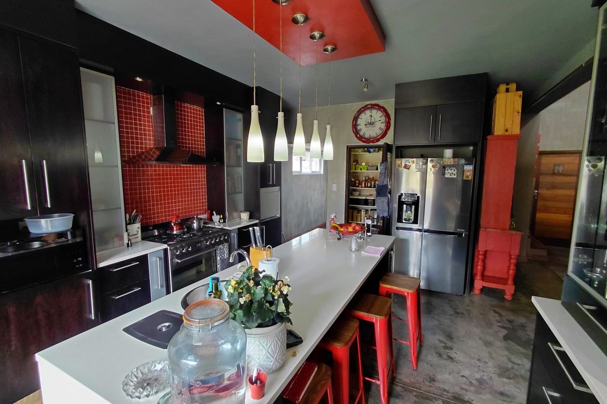 Modern kitchen featuring a large central island, dark cabinetry, red tiled backsplash, and a striking red bulkhead ceiling with pendant lighting.
