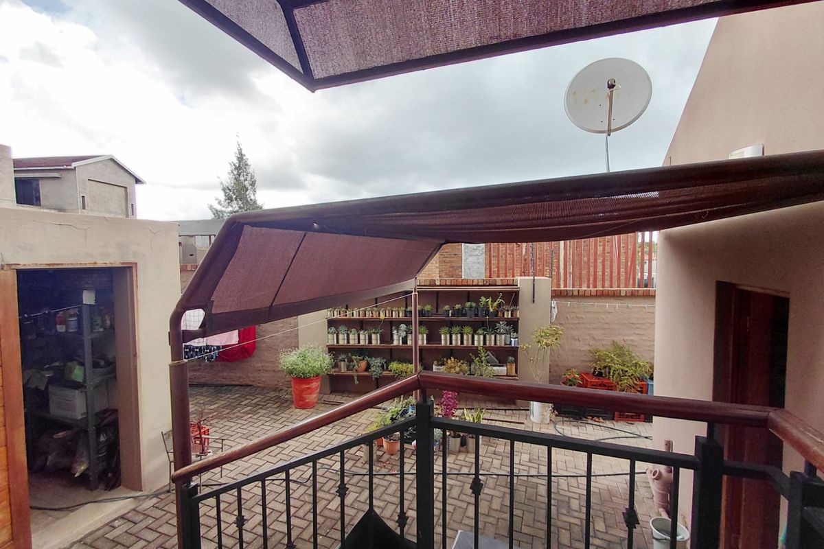 A paved rear courtyard area featuring a metal railing, a retractable shade awning, and built-in shelving against the boundary wall.