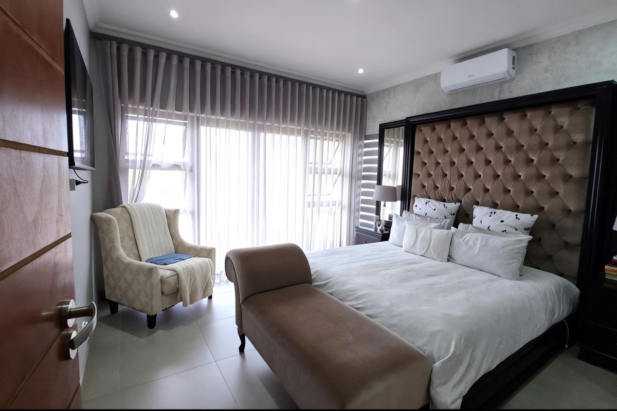 Spacious bedroom featuring tiled flooring, recessed ceiling lighting, and a wall-mounted air conditioning unit, with large sliding doors leading to an outdoor area.