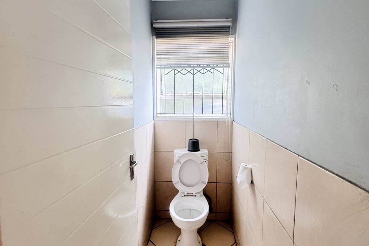 A compact, functional guest toilet featuring tiled flooring, half-tiled walls, and a window with security bars for added safety.