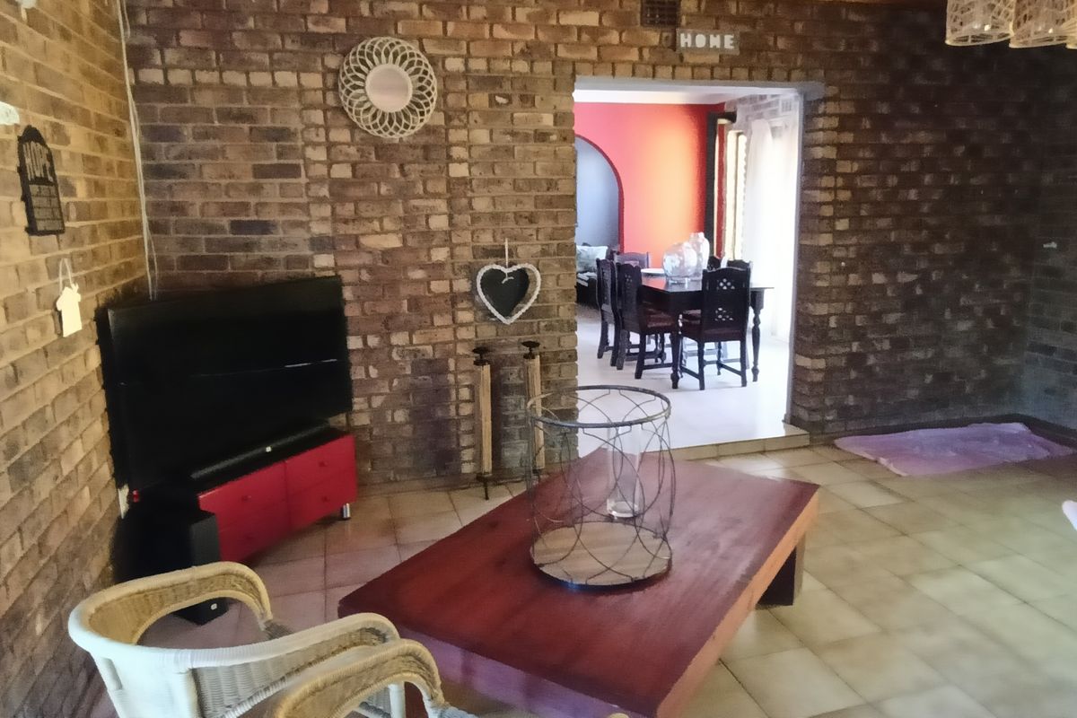 A living room featuring exposed brick walls and tiled flooring, with an open-plan transition into an adjacent dining area.
