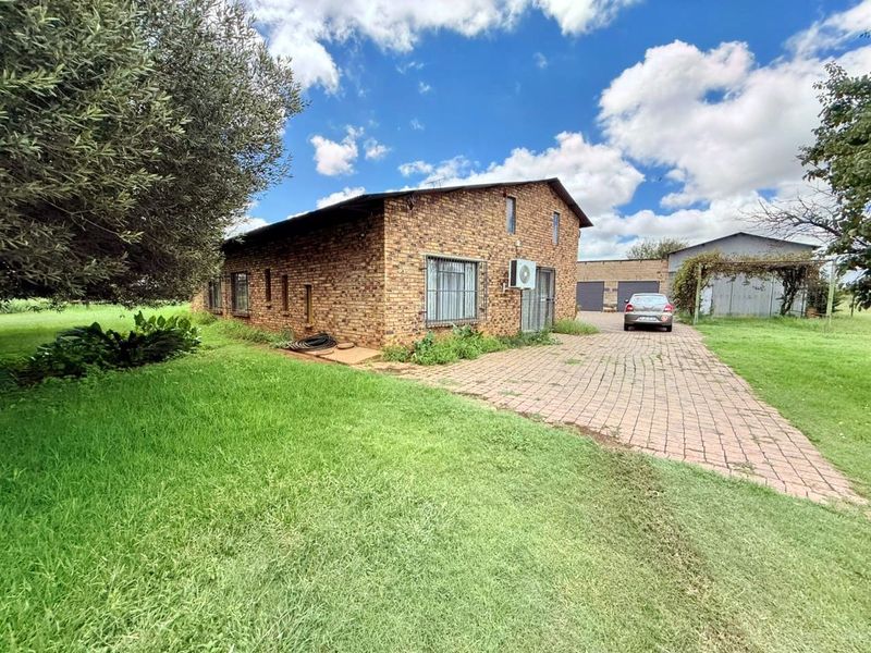 Exterior view of a face-brick house featuring a paved driveway, security bars on windows, and an outdoor air conditioning unit.
