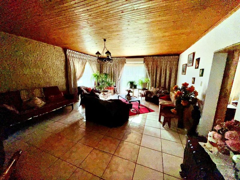 Spacious living room featuring a wood-paneled ceiling, tiled flooring, and a textured feature wall, offering a traditional layout with ample natural light.