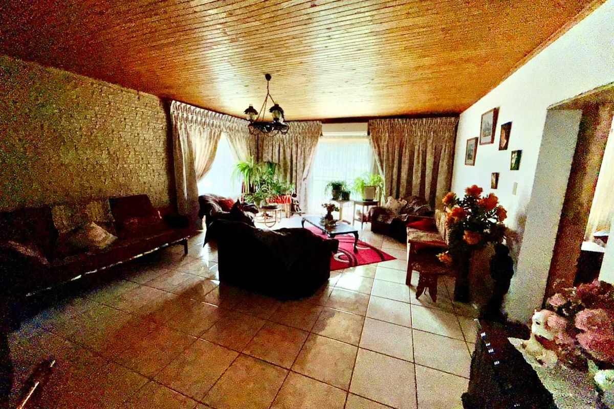 Spacious living room featuring a wood-paneled ceiling, tiled flooring, and a textured feature wall, offering a traditional layout with ample natural light.
