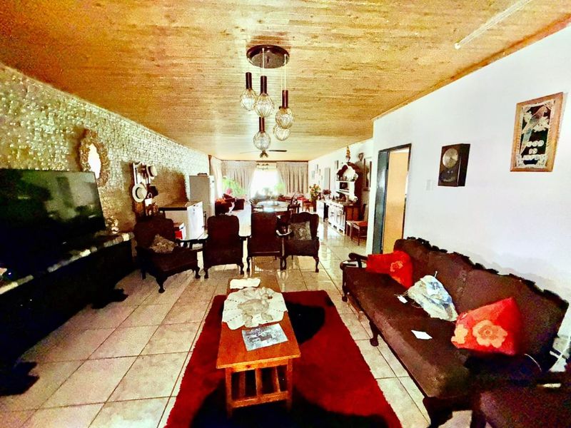 Spacious open-plan living and dining area featuring tiled flooring, a textured feature wall, and a wood-paneled ceiling with pendant lighting.