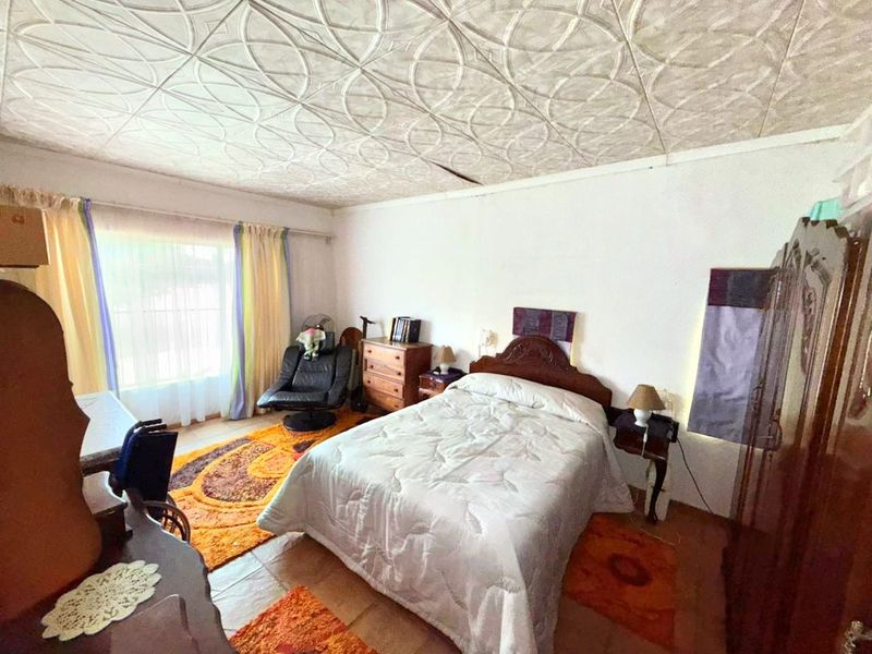 A bedroom featuring tiled flooring and a decorative patterned ceiling, offering a functional space with natural light from the window.