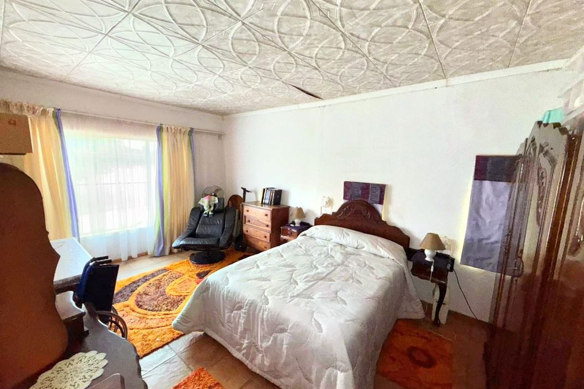 A bedroom featuring tiled flooring and a decorative patterned ceiling, offering a functional space with natural light from the window.