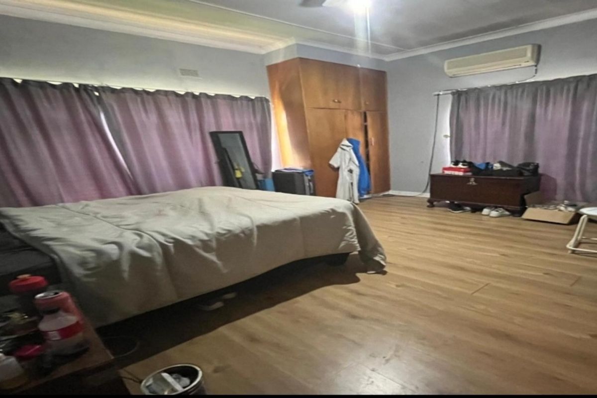 Spacious bedroom featuring wood-look laminate flooring, built-in wooden cupboards, and a wall-mounted air conditioning unit.